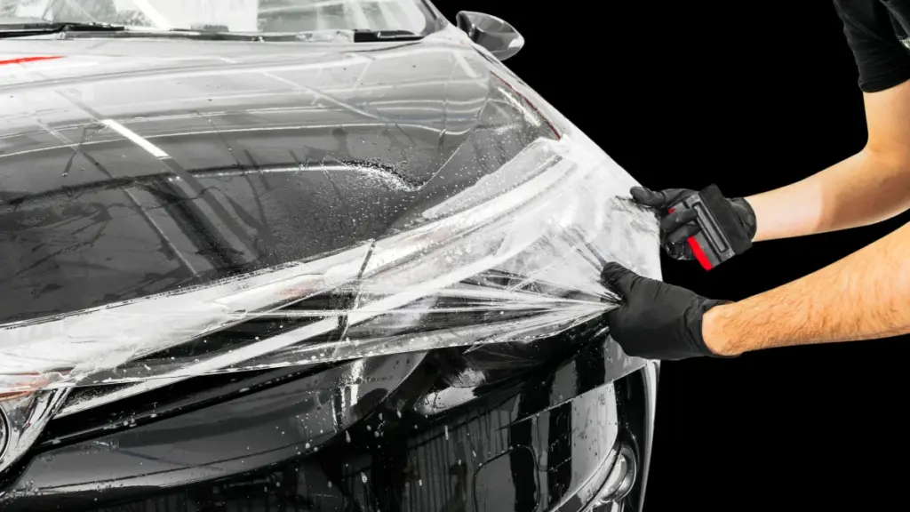 Profissional de luvas aplicando película transparente de proteção sobre o capô de um carro preto
